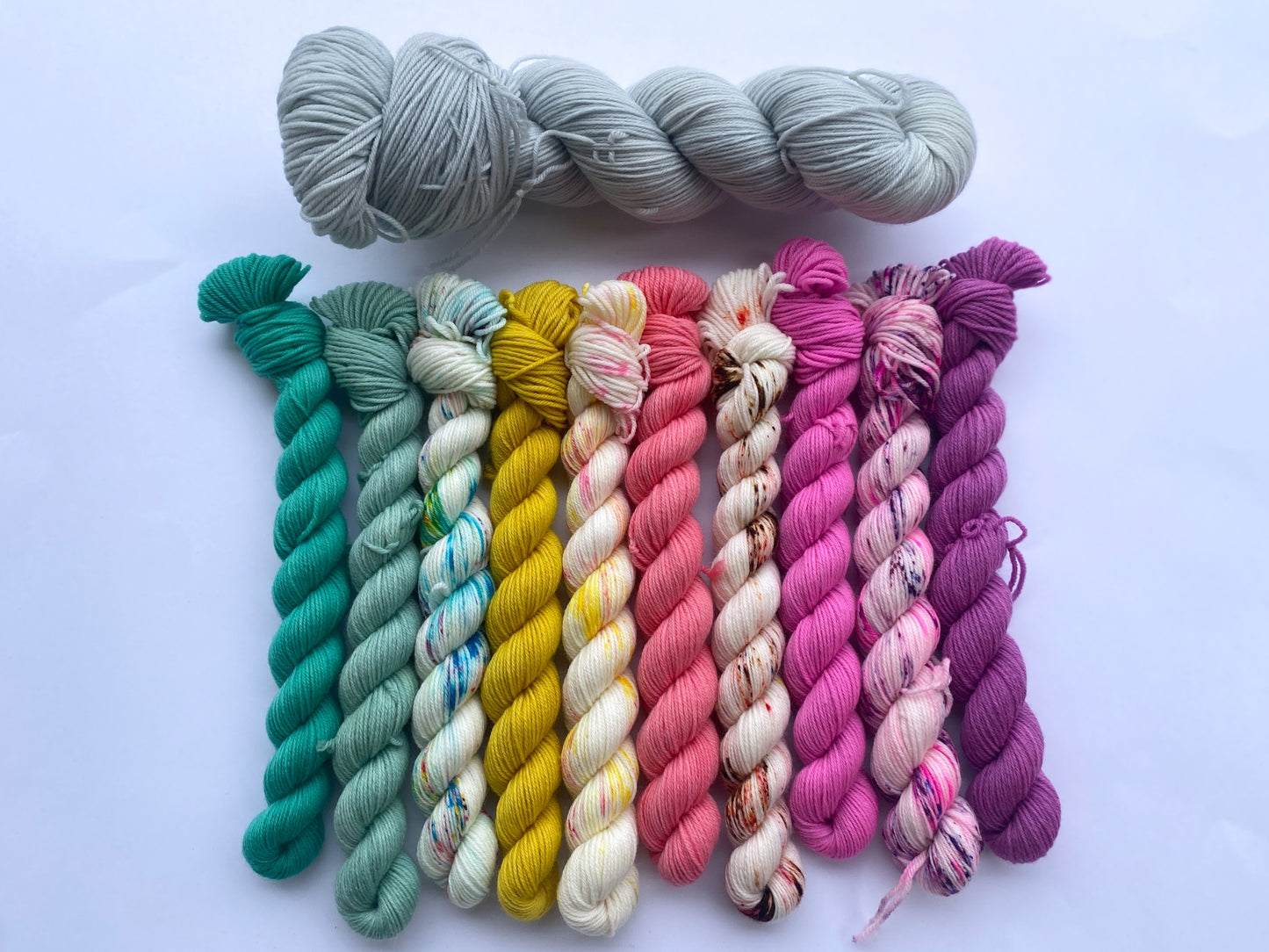 picture of one 3.5 oz skein of icy blue yarn atop 10 mini skeins of colorful yarn.